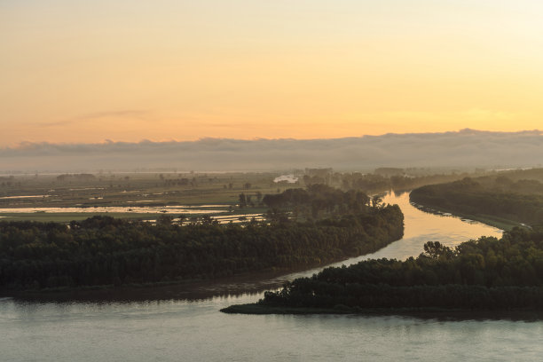 宽阔的河流沿岸流着森林和薄雾。河道环绕岛屿流动。晨光倒映在水面上。绚丽多彩的早晨，神秘大气的自然景观，雄伟壮观。图片下载