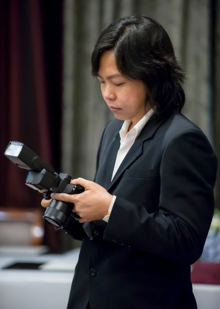 亚洲长发摄影师在海军蓝西装集中与他的相机。图片下载