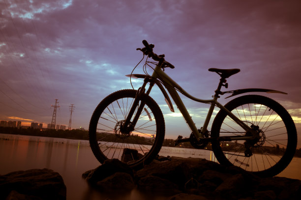 在自行车的傍晚，太阳在自行车上方，以夕阳和河流为背景图片下载