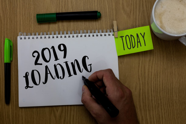 书写说明显示2019年加载。商业照片展示广告即将到来的一年预测未来的事件男人拿着马克笔笔记本衣服别针提醒木制桌子杯子咖啡。图片下载