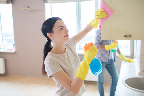 一个女孩用粉红色的抹布清洁衣柜表面的照片。她的丈夫站着，向前做着同样的事情。人们都集中图片下载