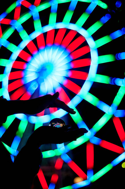 摩天轮穿过你手掌上的玻璃球。庆祝和休息的气氛。晚上冒险。明亮的颜色。手的轮廓图片下载