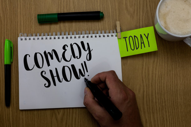写纸条展示喜剧表演。商业图片展示搞笑节目幽默搞笑的娱乐媒体男人拿着马克笔，笔记本，衣服，别针提醒，木桌，杯子，咖啡。图片下载