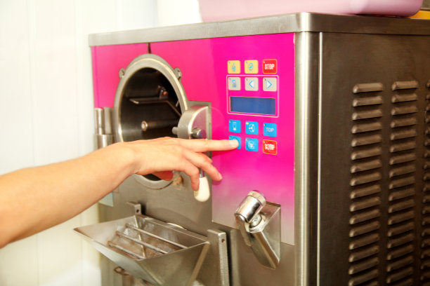 在雪糕厂，穿着厨师制服的女制糖员用雪糕机制作雪糕。女人是按下启动按钮和编程的生产冰淇淋机电脑。图片下载