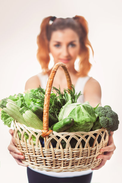 美丽的白人女孩抱着一篮子新鲜的生绿色蔬菜孤立。图片下载