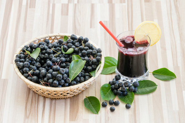 新鲜的野樱桃汁或黑果Aronia黑果汁，加冰，柠檬和吸管。篮子里的浆果在木制背景上图片下载