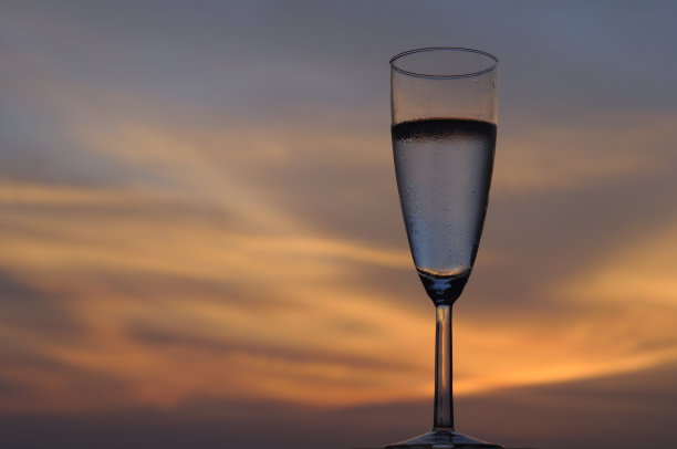 一杯气泡酒孤立在黄昏的天空背景下。图片下载