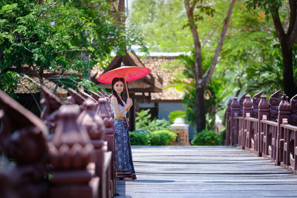 拿着雨伞的女人在行人桥上靠树行走图片下载
