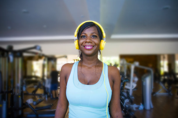 生活方式室内肖像在健身房的年轻快乐和迷人的美国黑人妇女在健身俱乐部听着音乐与耳机走在跑步机上愉快地训练图片下载