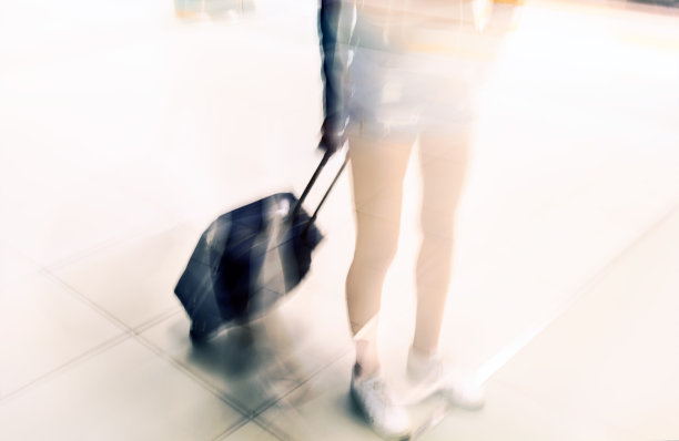 年轻的旅行者拖着行李箱在机场候机楼里走着去国外旅行。图片下载