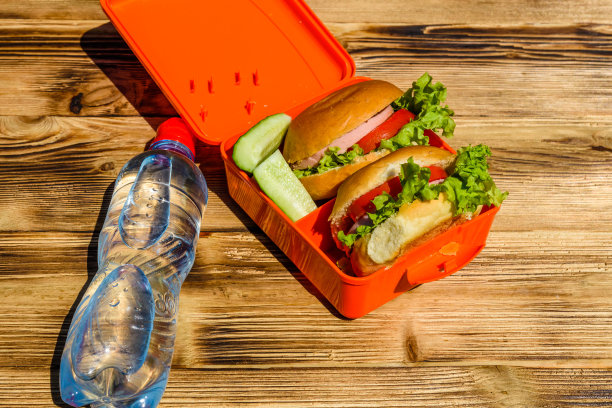 午餐盒里有带生菜的汉堡，木桌上有一瓶水图片下载