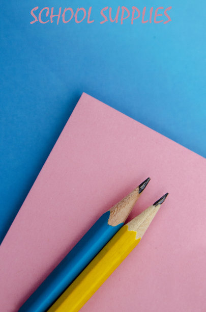 两支铅笔在粉红色的笔记本上，蓝色的纸上写着“学校用品”图片下载