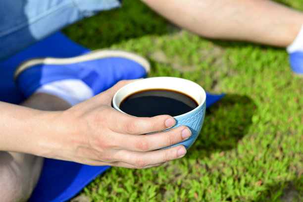 一个年轻人的手拿着一杯咖啡在户外的草地上图片下载