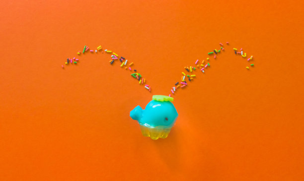 果冻状蓝鲸喷射彩色彩虹洒。俯视图上的橙色背景创意概念。图片下载