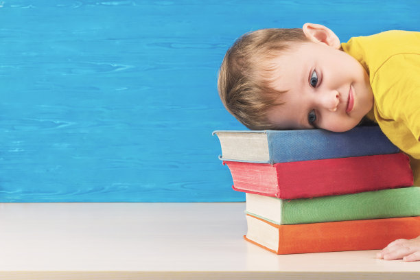 这个沮丧的小男孩把头搁在一堆课本上。回到学校。他不想做作业。图片下载