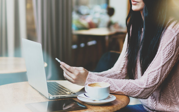 一位年轻的商务女性用智能手机上的应用程序查看明天的会议日程。一个女孩正在使用笔记本电脑和现代手机远程工作一个项目的裁剪照片图片下载