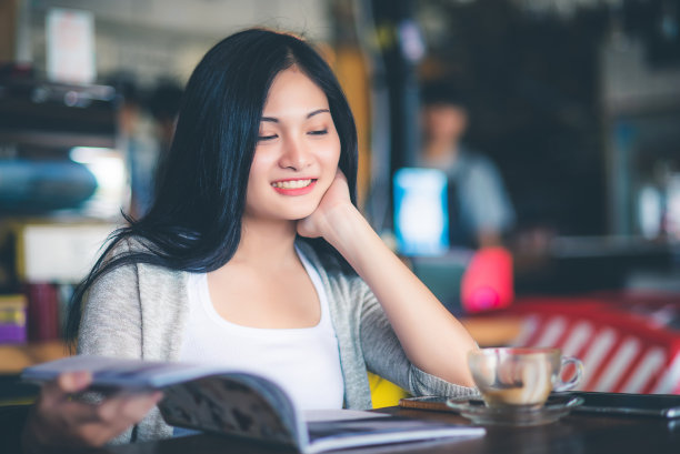 美丽迷人的年轻亚洲女人阅读一本杂志在早上的咖啡馆，复古的语调。图片下载
