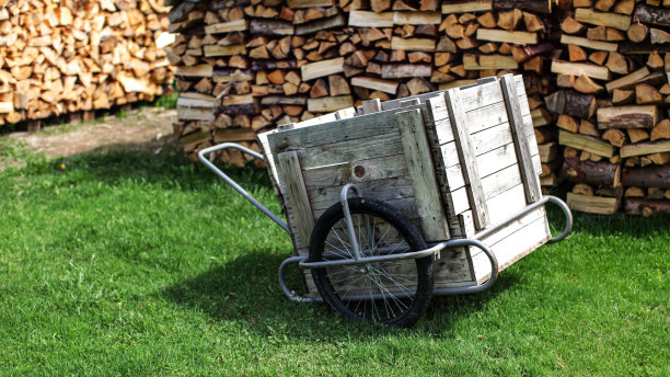 木头和钢车与橡胶轮胎，在绿色的草坪上，与成堆的劈柴堆放在后面。图片下载