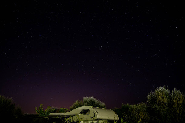 在繁星点点的夜晚，露营者在树林中露营。背景或壁纸与copyspace, RV自由的概念。图片下载