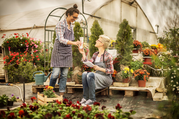 两个中年花匠正在后院休息，花房里满是五颜六色的鲜花。图片下载