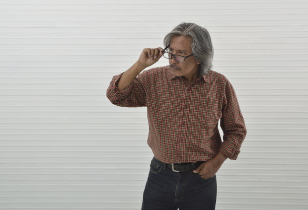 可疑的亚洲资深商人红色休闲衬衫和蓝色牛仔裤脱下眼镜图片下载