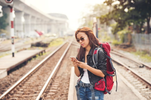 年轻女性旅行者和背包站在火车站使用智能手机图片下载