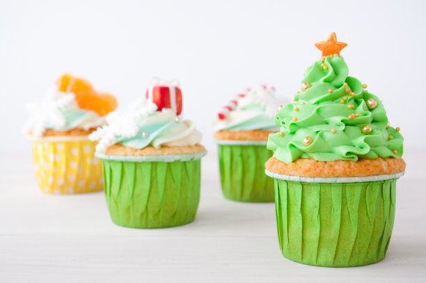 新年或圣诞节用鲜奶油做的绿色纸杯蛋糕，用圣诞树装饰，棒棒糖，雪花，红色盒子，橘子，银色和金色的糖果球放在白色背景上。图片下载