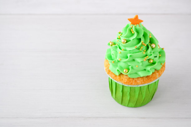 新年或圣诞绿杯蛋糕，用生奶油，装饰圣诞树，金色的糖果球和星星在白色的木头桌上。图片下载