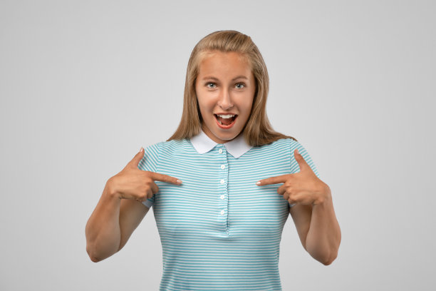 一个美丽快乐的十几岁女孩的图片，高兴地指着一件t恤，显示空间复制你的推广内容。图片下载