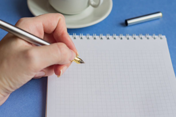 女用手握着笔，用一张空白笔记和一杯咖啡在蓝色背景上，选择性聚焦图片下载