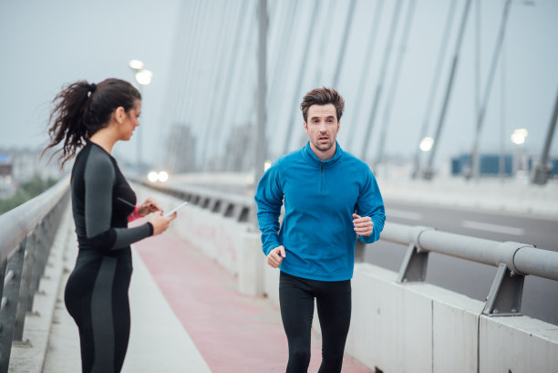 年轻女子拿着手机，看着慢跑者跑过图片下载