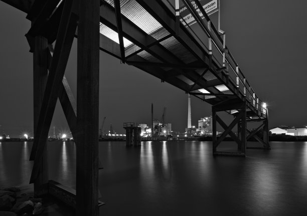 德国，不来梅——夜晚灯火通明的港口，上面是生锈的钢铁码头，灯光在水中反射，远处是各种各样的工厂(单色)图片下载