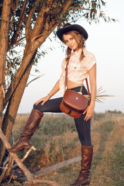 女牛仔女穿着牛仔裤靴子衬衫和一个袋子在一个盒子和一个轮子在一棵树上图片下载