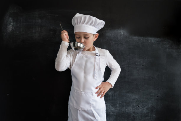 小男孩站在黑板旁检查汤。年轻的厨师的男孩。2019年日历创意设计理念。图片下载