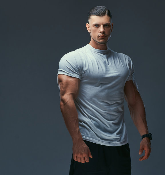 一个肌肉英俊的健美运动员的肖像在运动服摆姿势在一个工作室。孤立在灰色背景上。图片下载