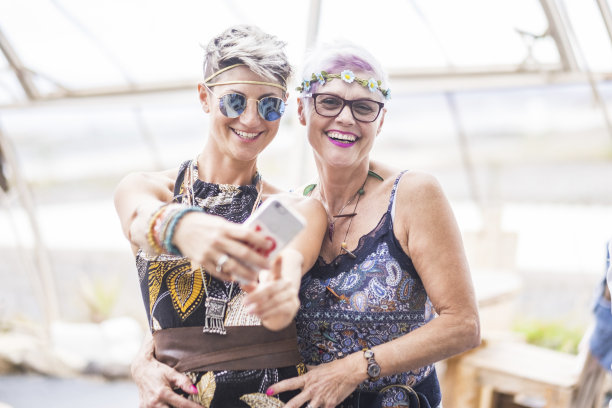 一对嬉皮士白种美女用智能手机。不同年龄的好有吸引力的人呆在一起在快乐的休闲活动与友谊。在社交上为快乐的老人和年轻的女士分享内容图片下载