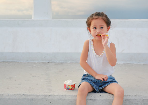 可爱的亚洲小女孩坐在户外，吃着杯里的冰淇淋。图片下载