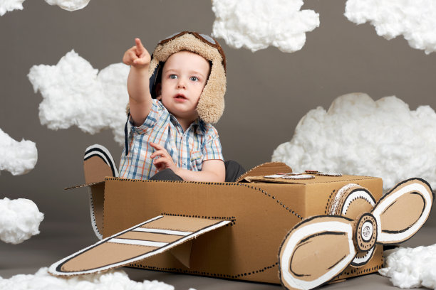小男孩在一架由硬纸板做的飞机上玩耍，梦想成为一名飞行员，灰色背景上是棉絮上的云朵，复古的风格图片下载