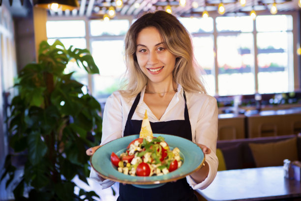 微笑的年轻女服务员拿着新鲜的沙拉对着商业厨房的服务员的肖像图片下载