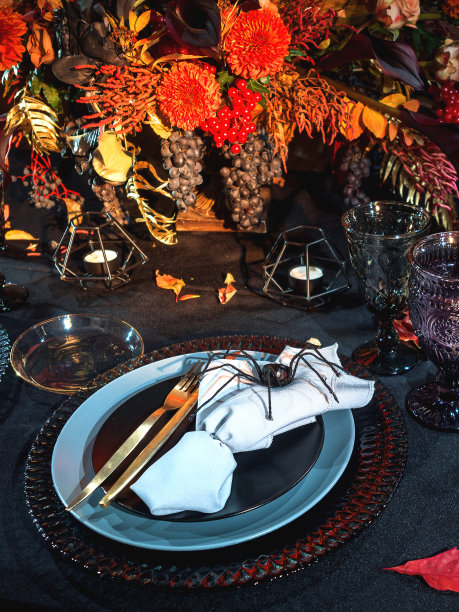 餐桌上的万圣节风格。黑色桌布上有红色的鲜花、装饰蜘蛛、刻有字母的南瓜和哥特式葡萄酒杯。节日装饰。图片下载