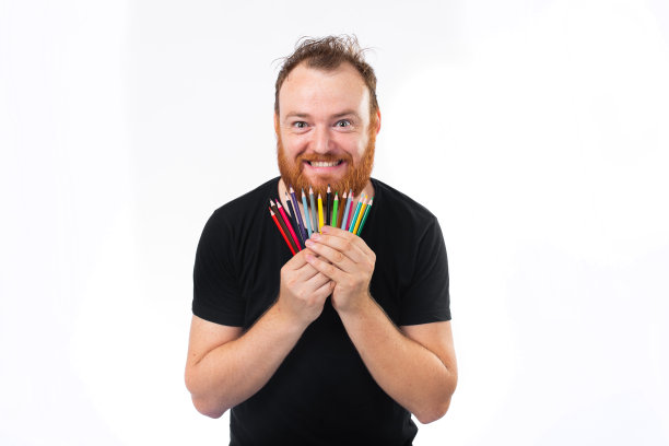 快乐的长胡子的成年人显示一堆彩色铅笔和微笑的相机孤立在白色的背景图片下载