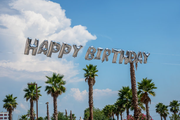 巨大的氦气球在空中写着庆祝生日的信件，还有棕榈树和蓝色的天空。图片下载