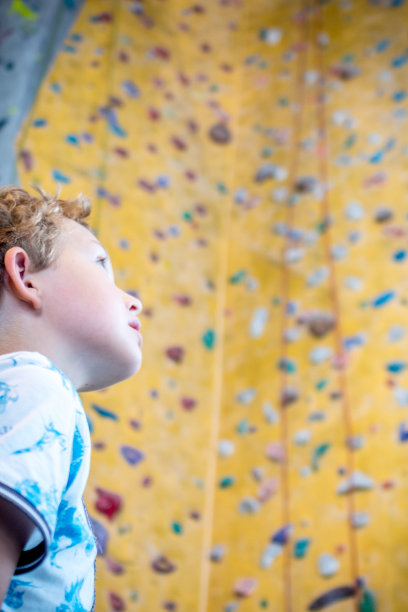 一个小男孩看着一条通往人造攀岩墙顶端的绳子，图片下载