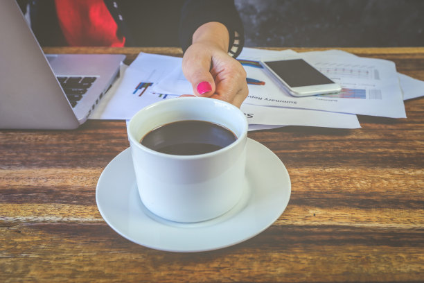 在办公室休息。办公室女性工作在笔记本电脑和拿着一杯咖啡，而坐在他的工作地点图片下载