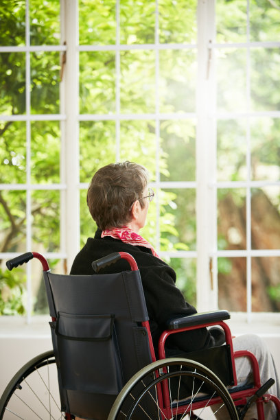 坐在轮椅上的沮丧女人透过窗户望向花园图片下载