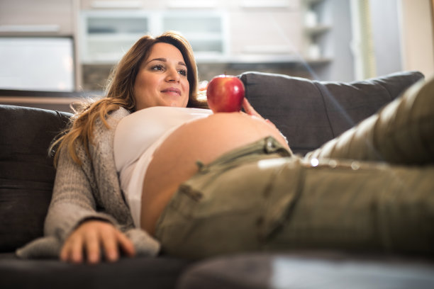 微笑期待女人拿着一个苹果在她的肚子上。图片下载