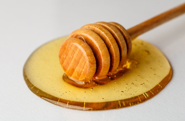 木制的蜂蜜滴和倾倒点蜂蜜在白色的背景，微距照片图片下载