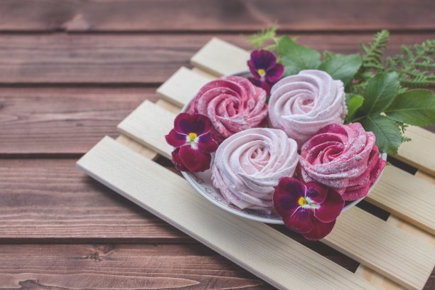 彩色的和风和花朵在深色的木制背景上。一套自制的白色和粉红色的和风或棉花糖在木制的背景。棉花糖、蛋白、西风,堇型花。本空间图片下载