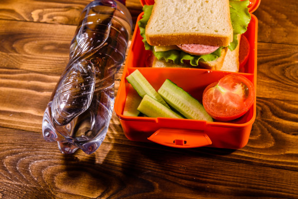木桌上有一瓶水和一盒三明治、黄瓜和西红柿图片下载