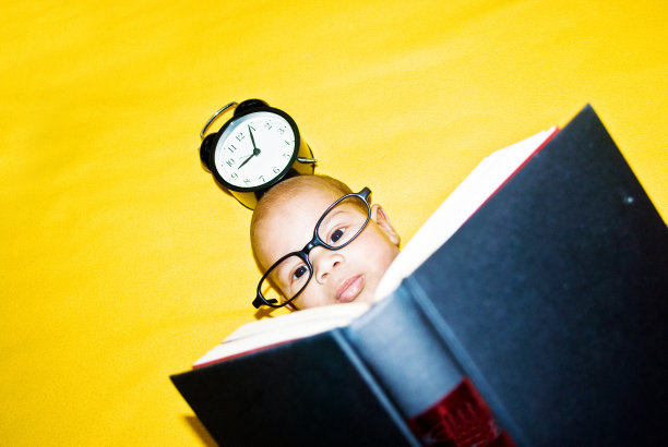 明日天才 - 戴着大眼镜的幼儿在彩色黄色背景上阅读大书图片下载